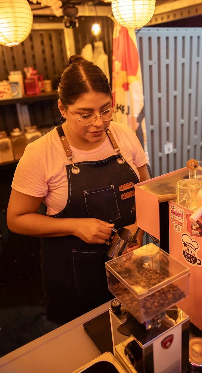 Barista de Hanami con delantal de mezclilla vaporizando leche junto a la máquina de espresso rosa.
